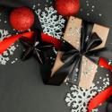 Red and Black Round tree ornaments, ribbon, and white snowflakes on a grey background.