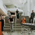 The Khemia Ensemble standing in staggered positions on stairs with their respective instruments